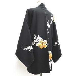 May include: A black haori jacket with white and gold embroidered floral designs. The flowers are stylized and resemble cherry blossoms.