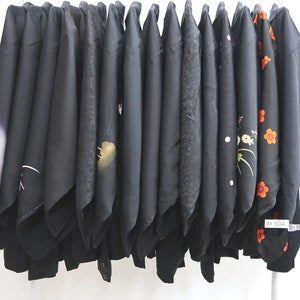 May include: A row of black silk kimonos with various floral patterns, including red and white flowers. The kimonos are hanging on a rack.