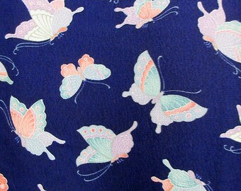 Könnte beinhalten: Ein marineblauer Stoff mit einem sich wiederholenden Muster aus rosa, weißen und grünen Schmetterlingen. Die Schmetterlinge sind stilisiert und haben einen zarten, fast märchenhaften Look.