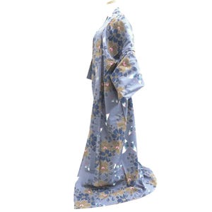 Op de afbeelding: Een lange, vloeiende kimono in blauwtinten, versierd met een bloemmotief in marineblauw, bruin en roze. Het kledingstuk heeft wijde mouwen en een wikkelontwerp, dat een traditionele Japanse esthetiek laat zien. De kimono wordt op een mannequin gepresenteerd.