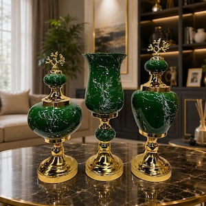 May include: A set of three decorative objects featuring deep green marble-patterned glass bodies with gold-toned metal bases and accents. Two pieces include lidded tops with gold coral-like finials, while the center piece is a tall glass vase.