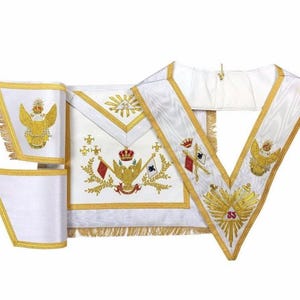 Puede incluir: Conjunto de regalia ceremonial blanco con detalles bordados en oro. El conjunto incluye un delantal, un cuello y puños, todos con intrincados diseños de coronas, águilas, banderas y rayos de sol. Los bordes están adornados con flecos dorados.