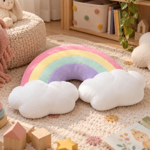 May include: A plush rainbow-shaped pillow featuring a curved arch with bands of pink, yellow, mint green, and lavender, anchored by two soft, white, cloud-shaped cushions on each end, creating a cohesive, multi-colored decorative accent piece.