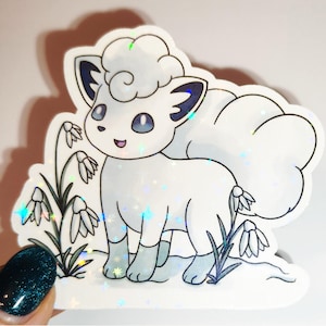 May include: A white sticker featuring a cartoon fox-like creature with fluffy fur and blue accents. The sticker has a holographic effect and is surrounded by stylized flowers and grass. The creature has blue eyes and is smiling.