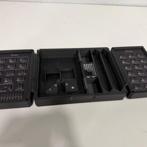 Pu&ograve; includere: Un organizer da tavolo nero pieghevole in tre parti, dotato di uno scomparto centrale e due pannelli laterali con quadranti meccanici integrati. Il pannello sinistro &egrave; etichettato Stats e quello destro Skills, entrambi con rotelle numeriche.