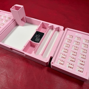 Pu&ograve; includere: Un organizer da tavolo per giochi in plastica rosa chiaro dotato di una torre per dadi, un vassoio centrale con una piccola gabbia nera per dadi e due pannelli laterali con quadranti rotanti etichettati con abilit&agrave; sotto la parola Skills.