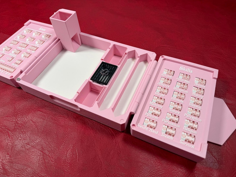 Pu&ograve; includere: Un organizer da tavolo per giochi in plastica rosa chiaro dotato di una torre per dadi, un vassoio centrale con una piccola gabbia nera per dadi e due pannelli laterali con quadranti rotanti etichettati con abilit&agrave; sotto la parola Skills.