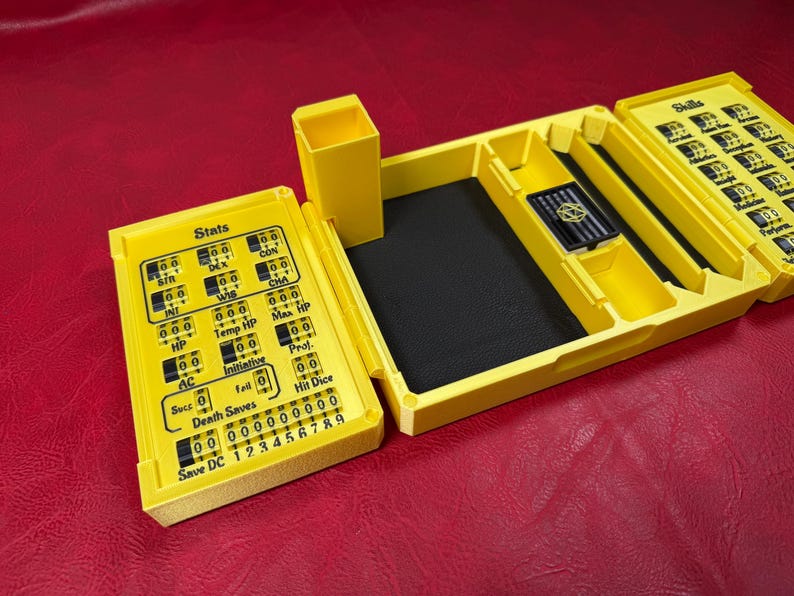 Pu&ograve; includere: Un organizer da tavolo in plastica giallo brillante con tracker meccanici integrati per le statistiche e le abilit&agrave; del personaggio. L'unit&agrave; include uno scomparto centrale foderato in nero, un portadadi verticale e quadranti numerici rotanti etichettati con testo come Stats, HP, AC e Skills.