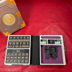 Può includere: Una custodia a forma di libro marrone e arancione con un emblema circolare sulla copertina, abbinata a un tracker di gioco aperto con pannelli bianchi e neri. Il tracker include scomparti etichettati per statistiche, abilità e dadi.