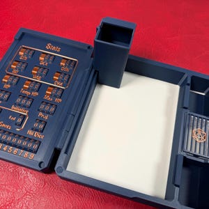 Pu&ograve; includere: Un organizer da tavolo in plastica blu scuro con un tracker meccanico delle statistiche integrato, numeri ed etichette color rame che includono Stats, STR, DEX, CON, INT, WIS, CHA, HP, Temp HP, Max HP, AC, Initiative, Proj, Death Saves e Hit Dice.
