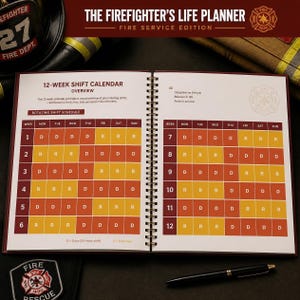May include: A spiral-bound planner titled The Firefighter's Life Planner Fire Service Edition, featuring a 12-week shift calendar with a grid of orange and yellow cells labeled D for days and R for rest days, alongside a black pen and fire gear.
