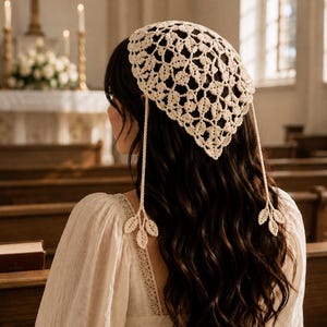 May include: An off-white triangular head covering crafted from intricate crochet lace featuring a repeating leaf pattern. The headpiece includes two long, thin braided ties that hang down, each finished with a small three-leaf crochet motif at the end.