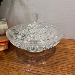 May include: A clear, glass candy dish with a lid. The dish has a textured, diamond-like pattern on the lid and bowl. The base of the bowl has a ribbed design. The lid has a small, decorative handle.