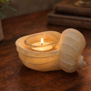 May include: A white ceramic mug with a black handle and the text "But First, Coffee" in a bold, black font. The mug is set against a blurred background, suggesting a cozy setting.