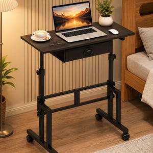 May include: A height-adjustable rolling desk with a dark wood-grain surface and a single storage drawer. The frame is constructed from black metal with four caster wheels, featuring adjustable knobs on the vertical supports for height modification.