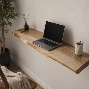 Könnte beinhalten: Ein wandmontierter Schwebeschreibtisch aus naturfarbenem, hellbraunem Holz mit einer Baumkanten-Oberfläche. Auf der Schreibtischplatte stehen ein silberner Laptop, ein schwarzer Diffusor und ein weißer, gerippter Keramikbecher mit zwei Stiften.