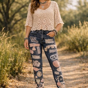 Puede incluir: Un top de ganchillo beige con mangas cortas y cuello en V combinado con vaqueros azul oscuro que presentan varios parches, incluyendo encaje, ganchillo floral y motivos de relojes. El conjunto se completa con un sombrero fedora beige y botines.