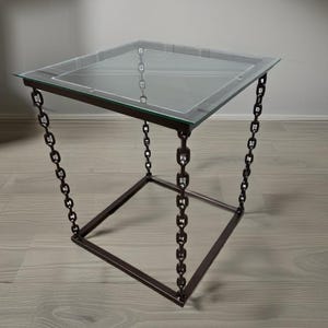 May include: A modern square coffee table with a clear glass top and a dark brown metal frame. The table's legs are formed by chains suspended from the corners, creating a unique and industrial design. The table measures approximately 30 inches in length and width.