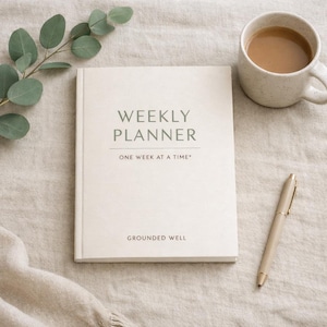 Könnte beinhalten: Ein cremefarbener Wochenplaner mit dem Text "WEEKLY PLANNER" und "ONE WEEK AT A TIME" in einer minimalistischen Schriftart. Ein beiger Stift und eine Tasse Kaffee liegen neben dem Planer. Ein Zweig mit grünen Blättern befindet sich in der oberen linken Ecke.