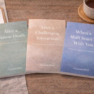 May include: Three books with soft-colored covers are displayed on a wooden surface. The titles read: "After a Patient Death", "After a Challenging Interaction", and "When a Shift Stays With You". A cup of tea and a clipboard with a pen are also visible.