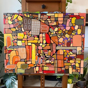 Könnte beinhalten: Abstraktes Gemälde auf Leinwand mit einem Mosaik aus Formen in warmen Farben wie Orange, Gelb und Braun, mit Akzenten in Rot und Lila. Das Kunstwerk wird auf einer Holzstaffelei präsentiert und erzeugt eine lebendige und moderne Ästhetik.