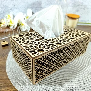 May include: A rectangular wooden tissue box with intricate geometric cutouts. The box is light brown with a dark brown trim and holds a stack of white tissues. The design features star and lattice patterns, adding a decorative touch to a functional item.