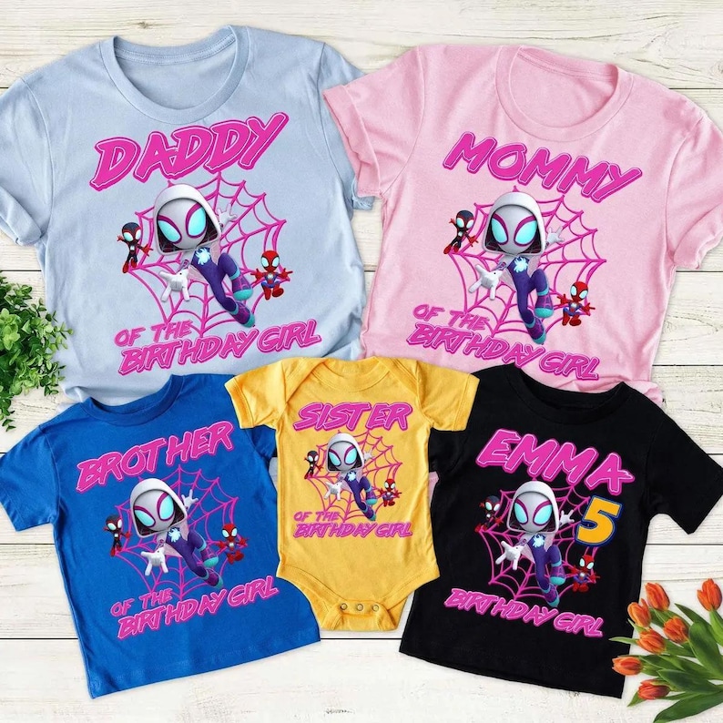 May include: A collection of colorful t-shirts and a onesie featuring a cartoon character in a spider web design. The shirts are light blue, pink, blue, yellow, and black, with text that reads "Daddy", "Mommy", "Brother", "Sister", and "Emma 5".