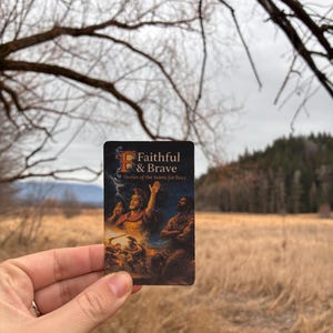May include: A small, rectangular card with the text "Faithful & Brave" and "Stories of the Saints for Boys." The card features a colorful illustration of religious figures. The background shows a field and trees.