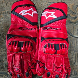 May include: Pair of red and black motorcycle gloves with the text "GP PRO" and a white star logo. The gloves have protective padding on the knuckles and fingers, and black accents. The gloves are made of leather.
