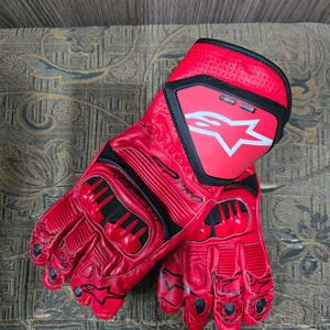 May include: A pair of red motorcycle gloves with black accents. The gloves feature a prominent white star logo on the cuff and the text "SP PRO". The gloves are made of a glossy material and have protective padding on the knuckles.
