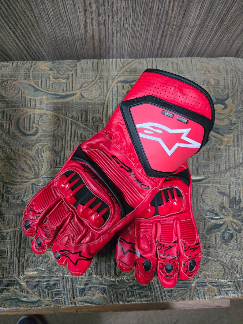 May include: A pair of red motorcycle gloves with black accents. The gloves feature a prominent white star logo on the cuff and the text "SP PRO". The gloves are made of a glossy material and have protective padding on the knuckles.