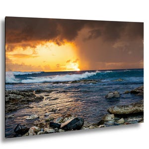 May include: A vibrant seascape print featuring a dramatic sunset over the ocean. The sky is filled with orange and dark clouds, with waves crashing against the rocky shore. The water reflects the golden light.