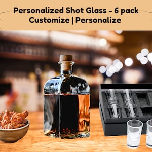 May include: Set of six personalized shot glasses in a black box with a clear glass bottle of dark liquid. The glasses are arranged in the box with two additional glasses on the table. The text on the box reads "Personalized Shot Glass - 6 pack Customize | Personalize".