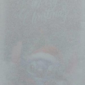 Könnte beinhalten: Verschwommenes Bild mit dem Schriftzug "Happy Christmas" in Schreibschrift. Unter dem Text ist eine Cartoonfigur mit Weihnachtsmütze zu sehen. Der Gesamteindruck ist weich und festlich.