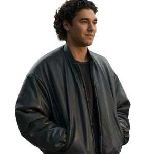 May include: A black bomber jacket with a smooth finish, featuring a stand-up collar, long sleeves with ribbed cuffs, and a central zipper closure. The jacket is worn over a dark charcoal gray shirt, showcasing a clean and structured silhouette.