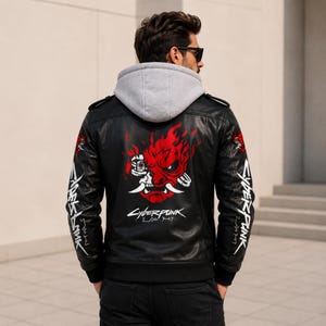 May include: A black leather jacket with a gray hooded sweatshirt layer underneath. The back features a large red and white graphic of a stylized oni mask with flames and the text Cyberpunk 2077. Both sleeves display white Cyberpunk 2077 text.
