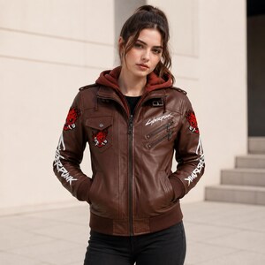 May include: A brown leather jacket featuring a dark red hood, a front zipper, and multiple pockets. The jacket displays white Cyberpunk text on the sleeves and chest, along with red and white graphic patches of a stylized face on the shoulders.