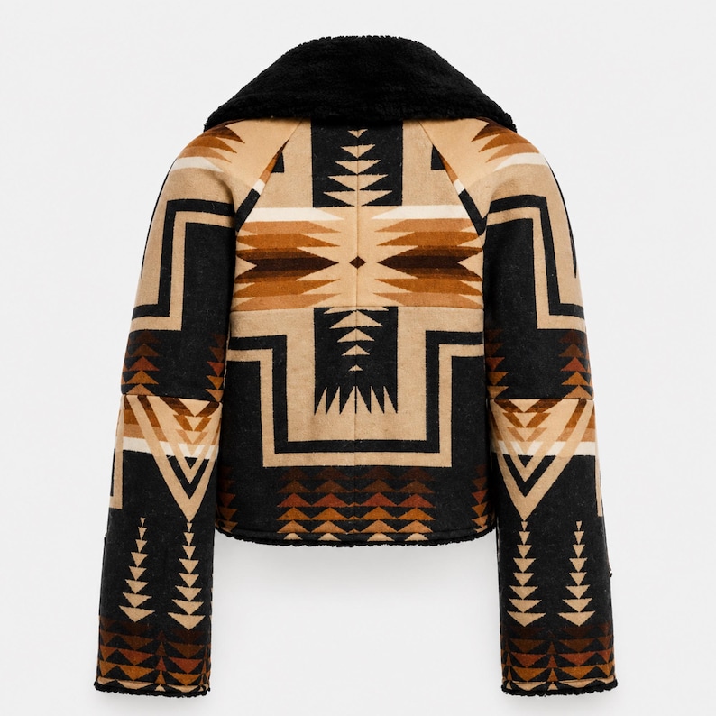 May include: A cropped jacket featuring a black faux fur collar and a geometric pattern in shades of tan, brown, and black. The design includes repeating triangular and chevron motifs across the back and sleeves, with a black hem and cuffs.