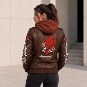 May include: A brown leather jacket with a hood, featuring a red and white graphic of a stylized robotic oni mask on the back. The text "CYBERPUNK" and "2007" are printed below the mask, with "CYBERPUNK" also printed vertically on both sleeves.