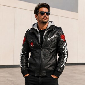 May include: A black jacket with a gray hood, featuring white Cyberpunk text on the sleeves and chest, red graphic patches on the shoulders, a front zipper, shoulder epaulets, and a chest pocket with a snap button closure.