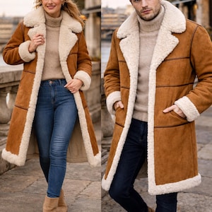 May include: A long, brown shearling coat with cream-colored shearling lining and trim. The coat features a classic design with a wide collar and cuffs. The coat is worn with blue jeans and a tan turtleneck.
