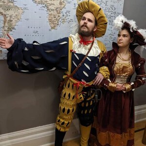 May include: Two people dressed in Renaissance-era costumes. The person on the left is wearing a yellow, black, and white costume with a feathered hat. The person on the right is wearing a burgundy and gold dress with a white feathered hat.