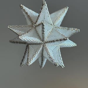 Può includere: Ornamento a forma di stella fatto a mano con perline bianche e dettagli argentati. La stella è a più punte e tridimensionale, con un design delicato e intricato. L'ornamento è sospeso da un filo d'argento.