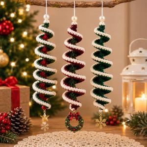 May include: Three spiral-shaped crochet ornaments hanging vertically. Each features a white yarn edge wrapped around a core of dark green or deep red yarn. Each ornament is topped with a white bead and finished with a gold-toned charm.