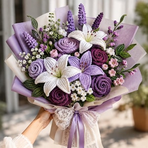 May include: A bouquet of crocheted flowers featuring white and purple lilies, dark purple and light purple roses, lavender sprigs, and small white blossoms with green leaves. The arrangement is wrapped in light purple paper and tied with a lace ribbon.