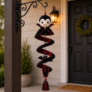 Pode incluir: Uma decoração suspensa em crochê com um personagem vampiro com capa preta e vermelha, um pequeno morcego preto e um pingente em forma de caixão com uma cruz vermelha. O design em espiral é acentuado com contas pretas, vermelhas e uma borla.
