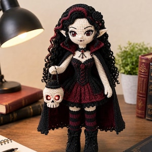 May include: A crocheted doll with long black hair, pointed ears, and red eyes, wearing a black and dark red dress with a high-collared cape. The doll features striped stockings, black boots, and holds a small crocheted skull lantern with glowing red eyes.