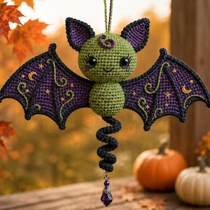 May include: A crocheted bat ornament with a round green head and body, large black eyes, and purple ears. The wings are dark purple with green embroidered stars and moons. A black spiral tail hangs from the bottom, ending in a purple crystal bead.