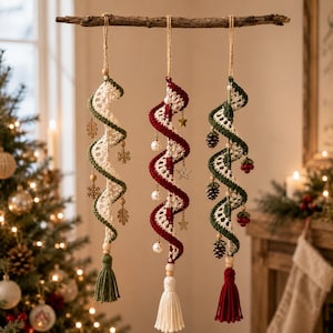 May include: Three hanging spiral ornaments suspended from a wooden branch. Each features crocheted yarn in white and green, white and red, or green and white. They are decorated with wooden beads, tassels, and charms including leaves, snowflakes, stars, pinecones, and berries.
