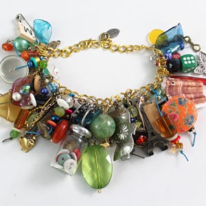 May include: A gold charm bracelet with a variety of colourful charms. Charms include beads, a miniature Eiffel Tower, a small jar with buttons, a butterfly, and a die. The bracelet is on a white background.